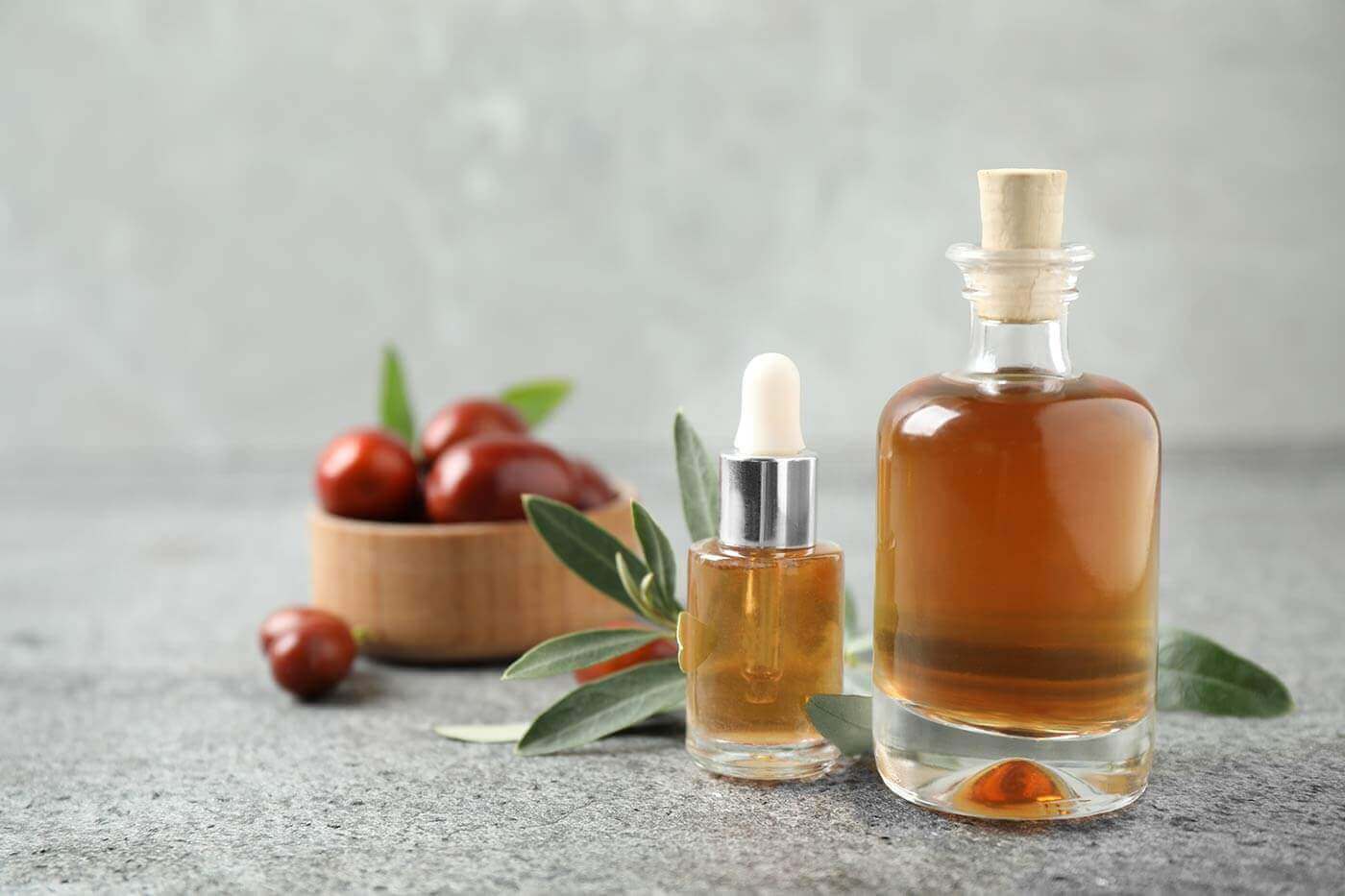 Glass bottles with jojoba oil on stone table against grey background