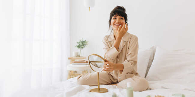 morning-skin-care-routine-at-night Woman in bed in pajamas applying morning skin care routine