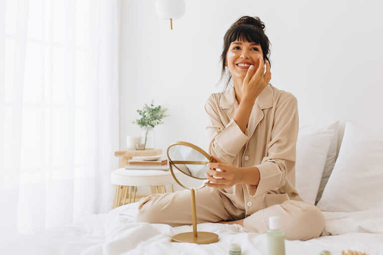 Woman in bed in pajamas applying morning skin care routine