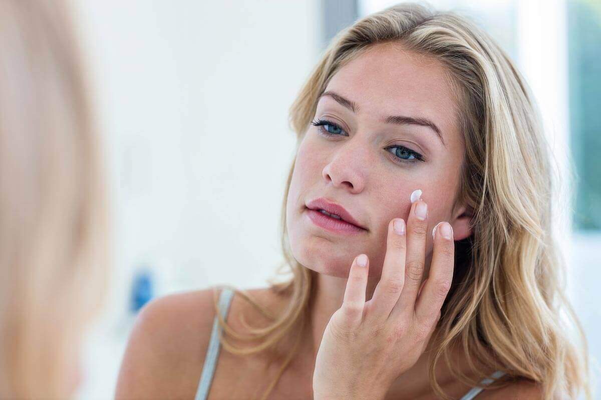 woman applying cream on her face in bathroom