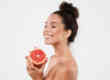 smiling woman with healthy glowing skin holding sliced grapefruit
