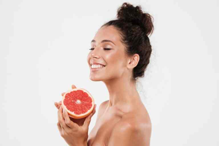 smiling woman with healthy glowing skin holding sliced grapefruit